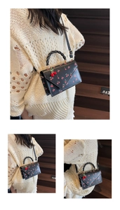 Detail of black cherry print leather bag with braided handle and cute charm on a sweater