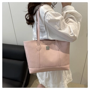 Detail of pink embossed leather tote bag with metal nameplate worn by a model