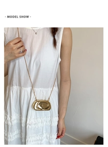 Macro detail of glossy gold geometric mini bag with delicate metal chain on white dress