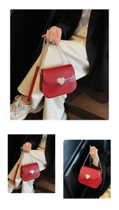 Close-up of shiny red leather saddle bag with gold heart clasp and metal chain strap