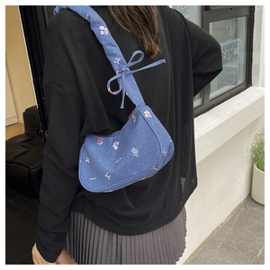Detail of blue denim underarm bag with pink floral embroidery and bow strap on model
