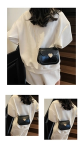 Detail of black patent leather crossbody bag with gold chain strap and silver heart buckle