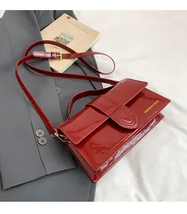 Detail of red glossy patent leather crossbody bag with adjustable gold metal buckle