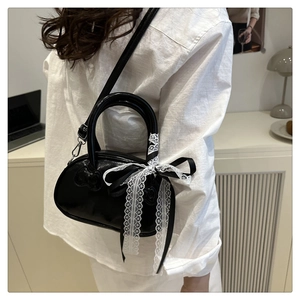 Detail of black patent leather handbag featuring a stylish white lace bow on the side