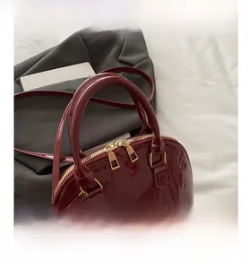 Close-up of glossy burgundy patent leather shell bag with gold double zippers and handles