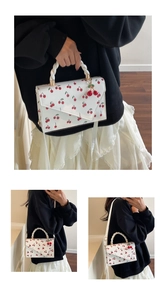 Detailed view of white cherry print handbag with 3D cherry charm and twisted rope handle