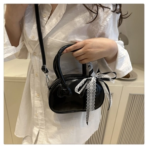 Detail of glossy black patent leather bag with cat embossing and lace polka dot bow