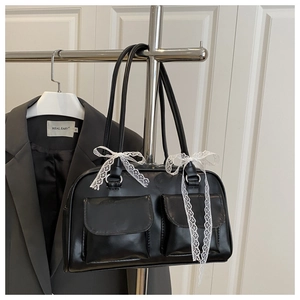 Detail of black leather handbag with white lace bow accents and front flap pockets