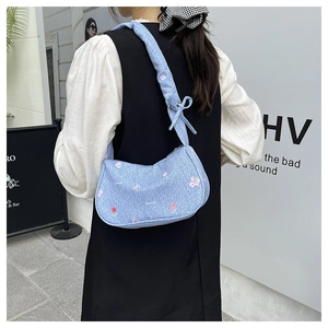 Detail of light blue denim bag with floral embroidery and decorative ribbon bow