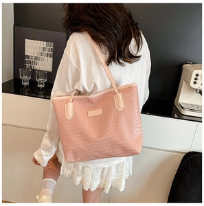 Detail of pink woven leather tote bag featuring a branded badge and shoulder strap