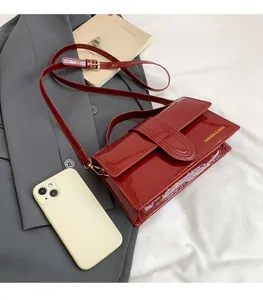 Detail of red patent leather handbag with gold lettering next to a smartphone for size scale