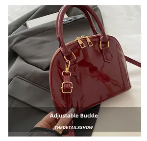 Detail of adjustable shoulder strap and gold hardware on burgundy patent shell bag
