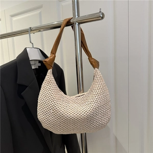 Handwoven cream straw hobo bag with knotted brown leather shoulder strap shown on hanger