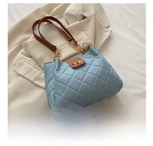 Close-up of sky blue quilted tote bag with brown leather strap and gold twist lock detail