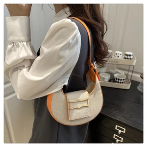 Detail of a chic orange and beige crescent shoulder bag with golden metallic hardware