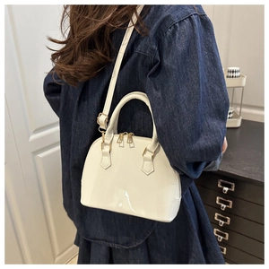 Close-up of white patent leather shell bag with gold zippers worn with a denim dress