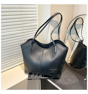 Detailed close-up of a minimalist black leather tote bag with a small FASHION logo tag