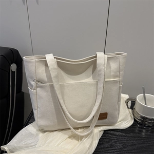 Minimalist canvas tote bag with brown leather label and wide shoulder strap in home setting