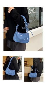 Detail of floral embroidery and creative cat text on a blue denim crescent shoulder bag