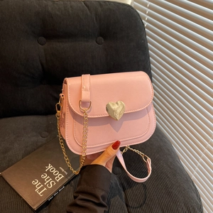 Pink crossbody bag with a large gold heart buckle and metal chain strap held by hand