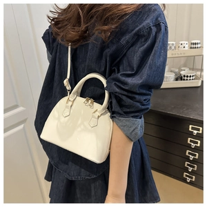 Close-up of white patent leather shell bag with dual metal zippers and top handle