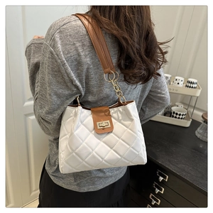 Detail of white quilted bag with brown leather strap and gold chain on shoulder