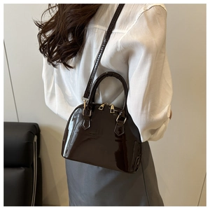 Detail of glossy dark brown shell bag with golden zipper and sleek top handle