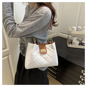 Close-up of white quilted bag with brown leather flap and golden metal twist lock