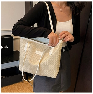 Close-up of beige woven texture tote bag featuring white handles and fashion logo patch