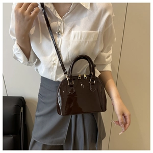 Detail showing deep brown glossy patent leather shell bag with gold-tone hardware