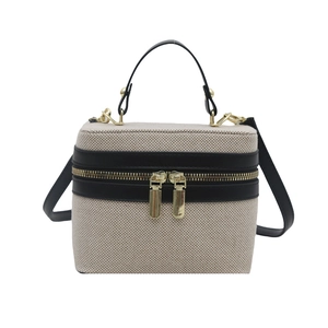 Beige woven box handbag with black leather trim and dual gold zippers on white background