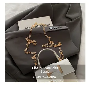 Detail shot of the golden chain strap and buckle on a white leather square handbag