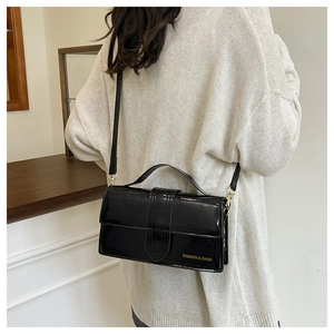 Detail view of black patent leather crossbody bag with golden Fashion & Bags logo lettering