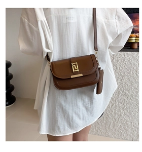 Close-up of brown leather saddle bag featuring a geometric gold clasp and adjustable strap