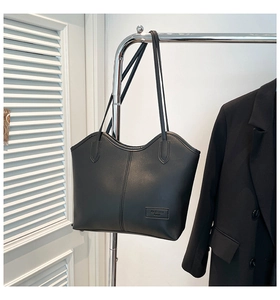 Detail of minimalist black leather tote bag with unique wavy edge and fashion logo patch