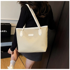 Detail of light beige woven tote bag with white straps and fashion leather label