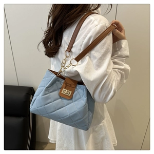 Detail of light blue quilted crossbody bag with gold chain strap worn by model