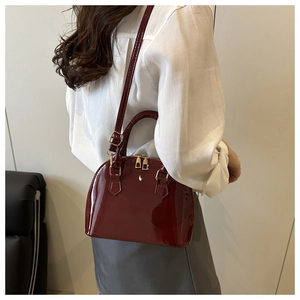 Model wearing a glossy burgundy patent leather shell bag with gold zippers and crossbody strap