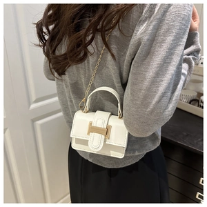 White mini crossbody bag with gold metal lock and chain strap shown on a model