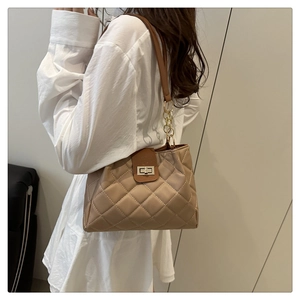Detail of the khaki quilted shoulder bag with metal chain strap worn by a model