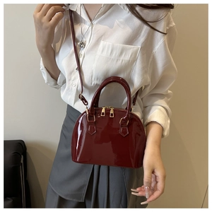 Close-up of burgundy patent leather shell bag with glossy finish and gold metal zippers