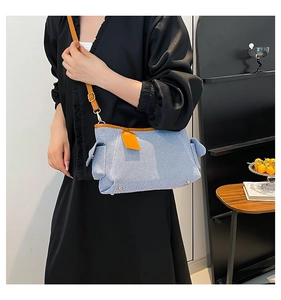 Dettaglio della borsa a tracolla in denim blu con finiture in pelle marrone e piedini in metallo