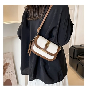 Detail of contrast stitching saddle bag with gold metal lock and leather leaf pendant