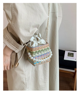 Detail of woven chain handbag with pearl handle and crossbody strap in a studio setting