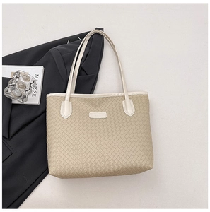 Close-up of beige woven tote bag detailing leather straps on a black blazer