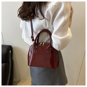 Detailed view of burgundy patent leather shell bag with gold hardware on a model