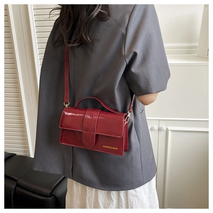 Detail of dark red patent leather crossbody bag with top handle worn on grey blazer
