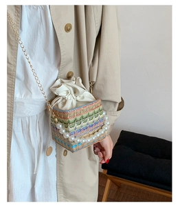 Close-up of colorful woven bucket bag with pearl handle and metal chain on a model
