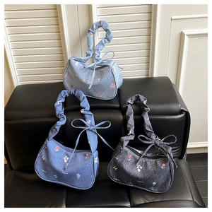 Detailed shot of three denim shoulder bags with floral embroidery and bow accents