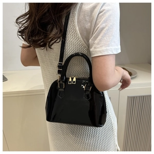 Glossy black patent shell bag detail with golden hardware and adjustable strap